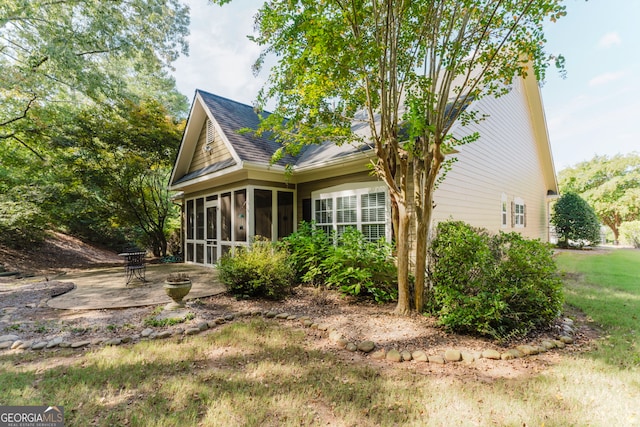 view of side of home with a sunroom, a lawn, and a patio area