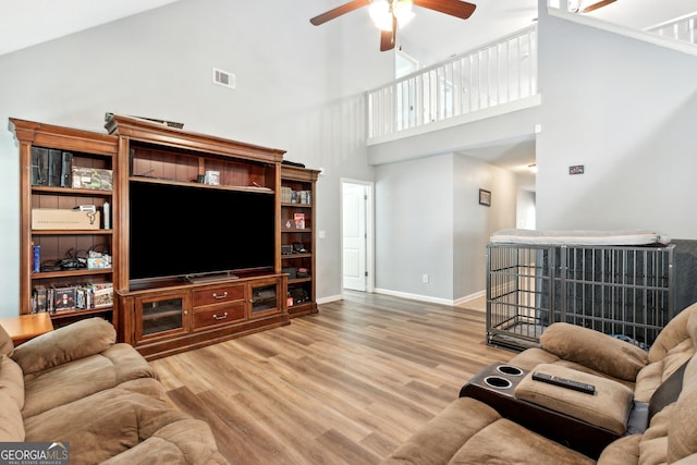 living room featuring ceiling fan, a high ceiling, and wood-type flooring