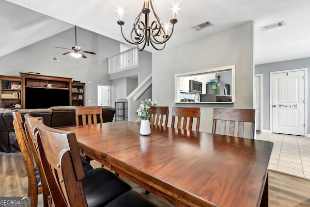 tiled dining space featuring high vaulted ceiling and ceiling fan with notable chandelier