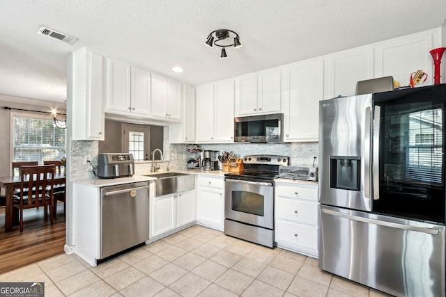 kitchen featuring stainless steel appliances, backsplash, light tile patterned floors, sink, and white cabinetry