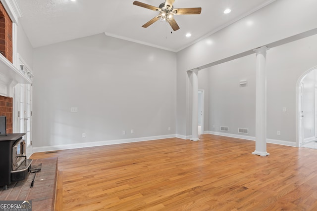 living room featuring lofted ceiling, light hardwood / wood-style flooring, a wood stove, ceiling fan, and ornate columns