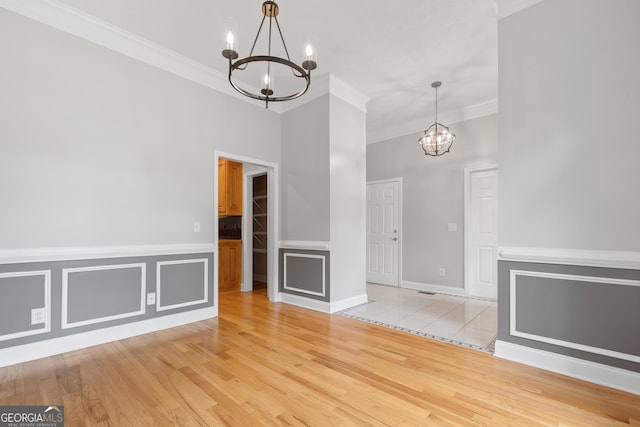 unfurnished dining area with ornamental molding, an inviting chandelier, and light hardwood / wood-style floors