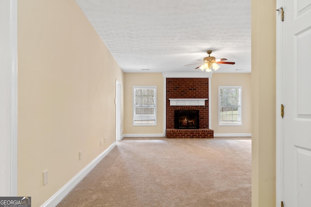 unfurnished living room with a textured ceiling, a brick fireplace, light colored carpet, and ceiling fan