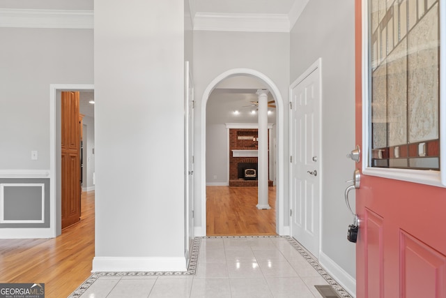 foyer with a brick fireplace, crown molding, ceiling fan, and light tile patterned floors