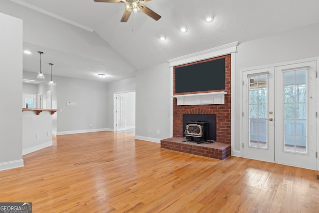 unfurnished living room featuring french doors, a wood stove, light hardwood / wood-style flooring, vaulted ceiling, and ceiling fan