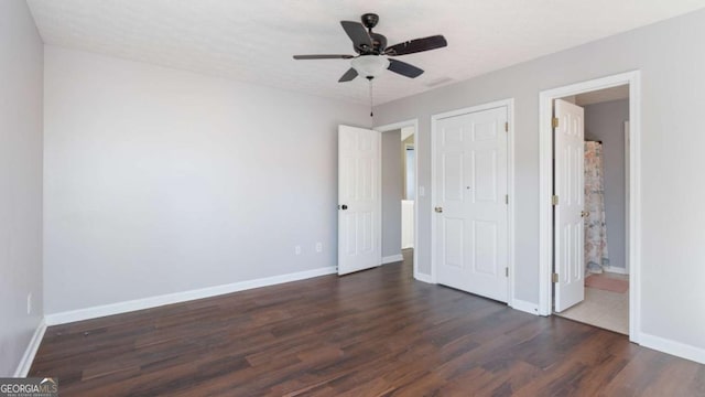 unfurnished bedroom featuring ensuite bath, a ceiling fan, dark wood-type flooring, and baseboards