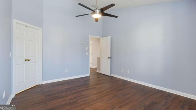 unfurnished bedroom featuring dark wood finished floors, baseboards, a towering ceiling, and ceiling fan