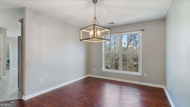 empty room with a notable chandelier, visible vents, baseboards, and wood finished floors