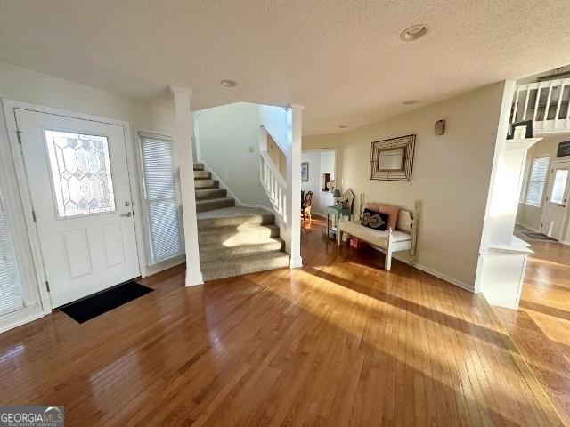 entrance foyer with ornate columns, stairs, wood finished floors, and a textured ceiling