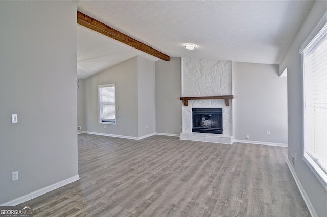 unfurnished living room with a fireplace, light hardwood / wood-style floors, vaulted ceiling with beams, and a textured ceiling