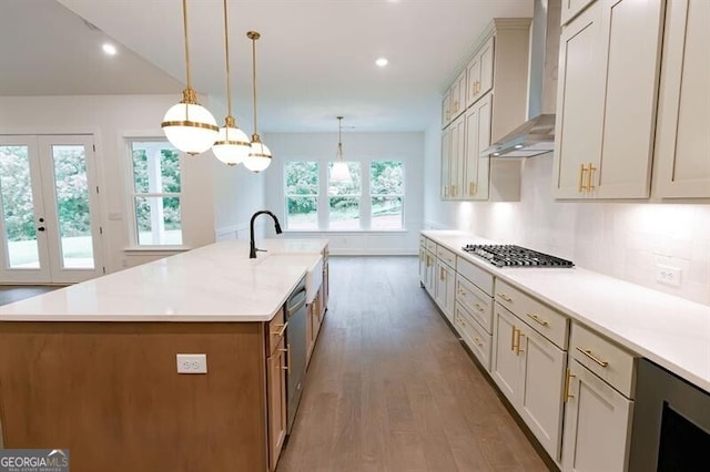 kitchen with decorative light fixtures, a large island with sink, sink, appliances with stainless steel finishes, and wall chimney exhaust hood