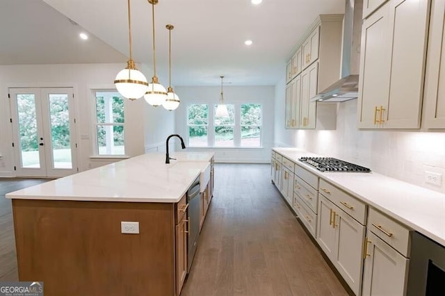 kitchen with stainless steel appliances, a large island with sink, wall chimney range hood, and hanging light fixtures