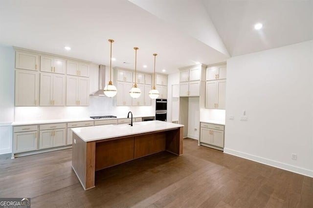 kitchen with gas stovetop, wall chimney exhaust hood, dark wood-type flooring, hanging light fixtures, and a kitchen island with sink