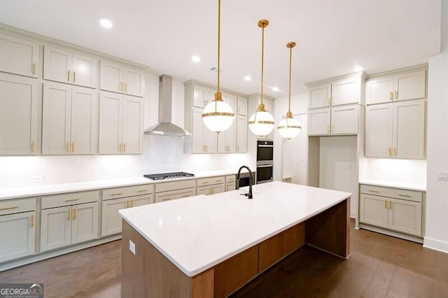 kitchen featuring appliances with stainless steel finishes, wall chimney exhaust hood, dark hardwood / wood-style floors, pendant lighting, and a kitchen island with sink