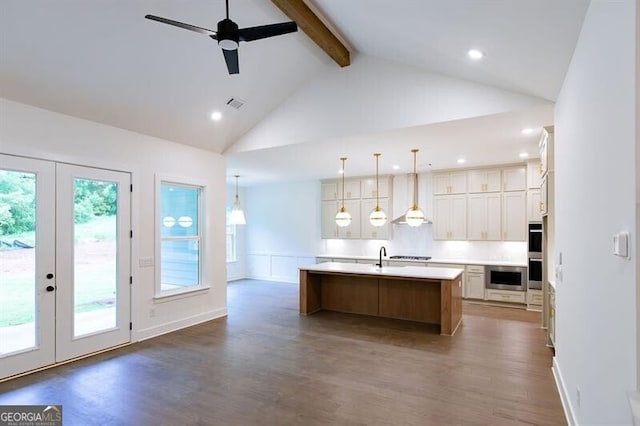 kitchen with beam ceiling, a kitchen island with sink, dark hardwood / wood-style flooring, and decorative light fixtures