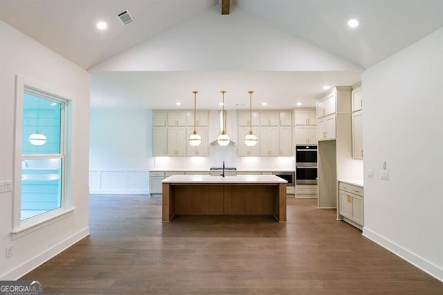 kitchen featuring stainless steel double oven, an island with sink, decorative light fixtures, dark hardwood / wood-style flooring, and sink