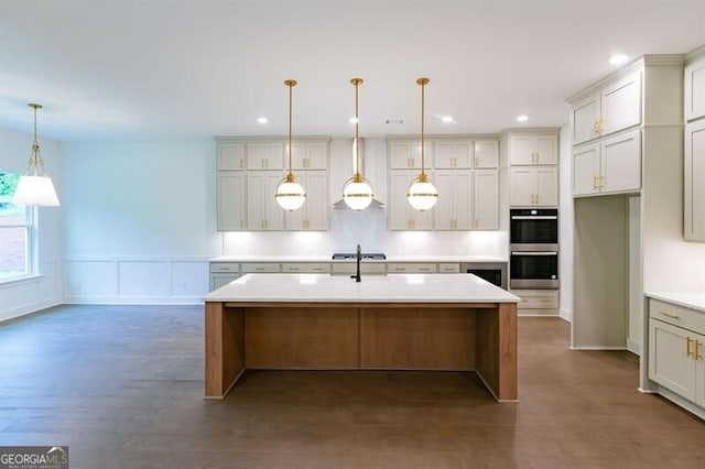 kitchen with pendant lighting, stainless steel appliances, wall chimney exhaust hood, dark hardwood / wood-style flooring, and a kitchen island with sink