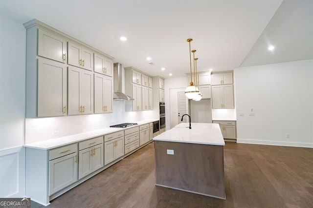 kitchen featuring wall chimney exhaust hood, stainless steel gas cooktop, decorative light fixtures, dark hardwood / wood-style flooring, and a kitchen island with sink