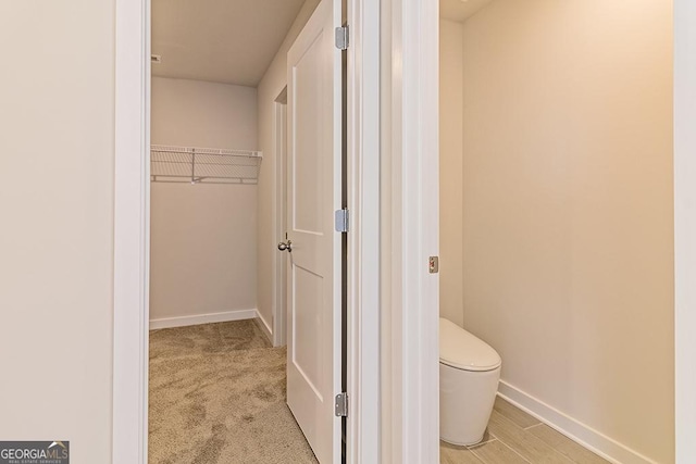 bathroom featuring baseboards, a spacious closet, and toilet