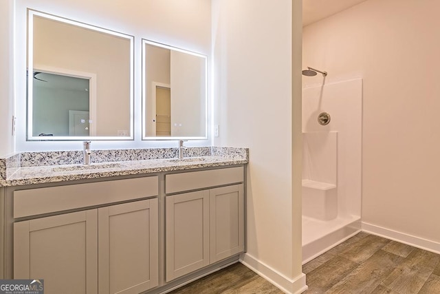 bathroom featuring double vanity, wood finished floors, a stall shower, and a sink