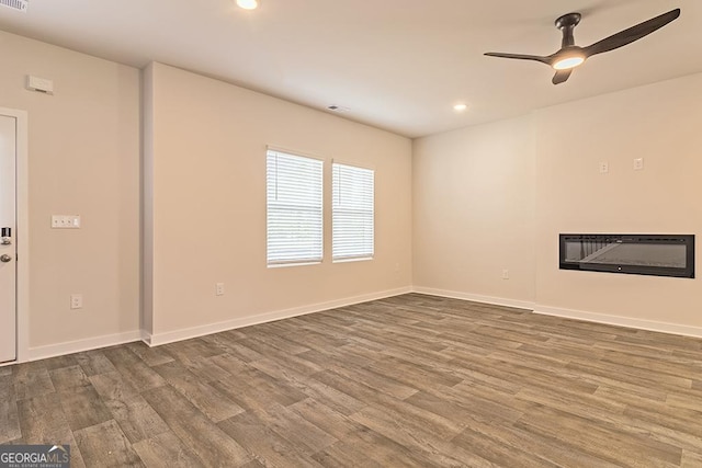 unfurnished living room featuring baseboards, a ceiling fan, a glass covered fireplace, wood finished floors, and recessed lighting