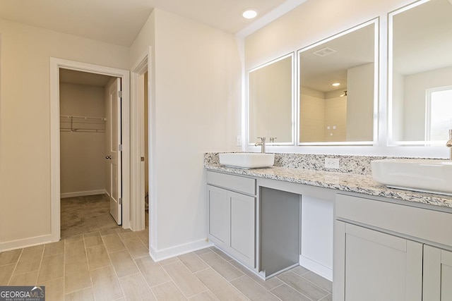 full bath featuring double vanity, baseboards, a walk in closet, and a sink