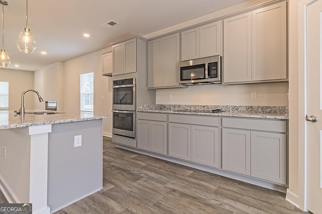 kitchen featuring light stone counters, stainless steel appliances, a sink, and gray cabinetry