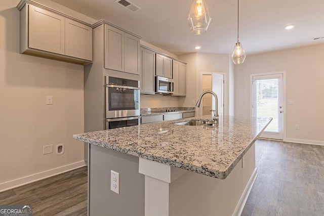 kitchen with a center island with sink, light stone counters, hanging light fixtures, stainless steel appliances, and a sink