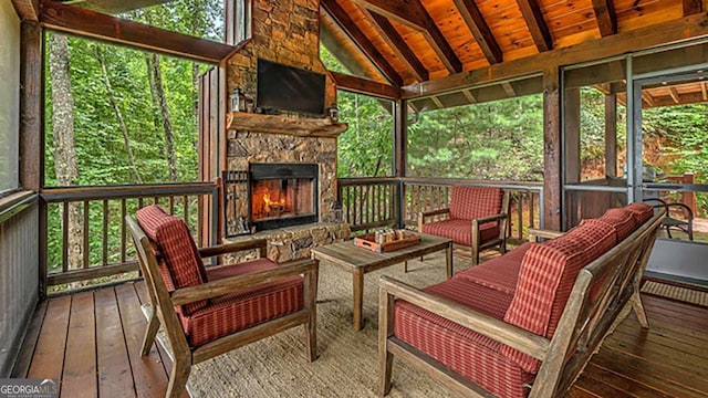 sunroom with plenty of natural light, lofted ceiling with beams, wood ceiling, and an outdoor stone fireplace