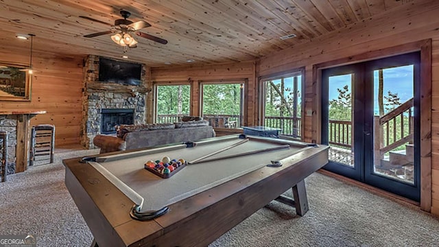 rec room featuring wood walls, a stone fireplace, carpet, ceiling fan, and wooden ceiling