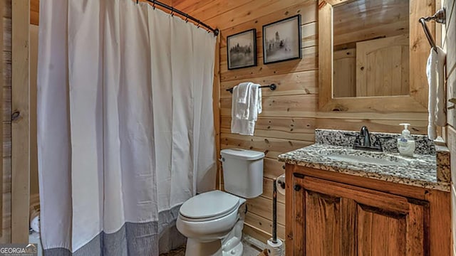 bathroom with toilet, vanity, and wood walls