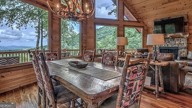 dining space with a stone fireplace, a chandelier, wood-type flooring, and wooden walls