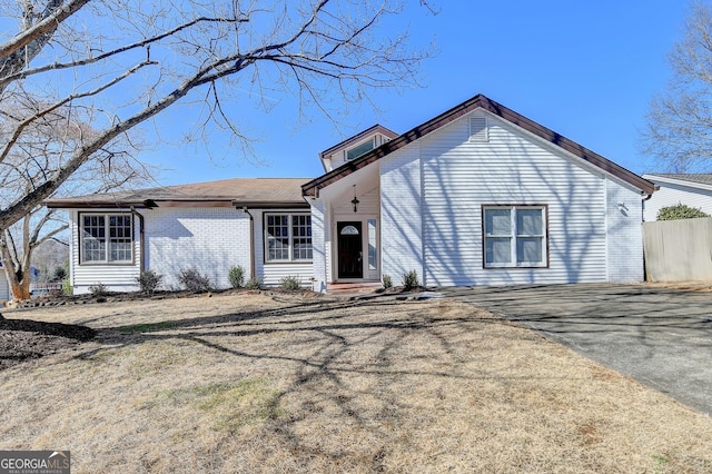 view of front of property with brick siding, driveway, and fence