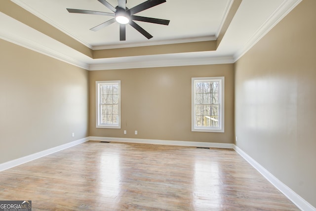 unfurnished room with visible vents, a tray ceiling, light wood-style flooring, and a wealth of natural light