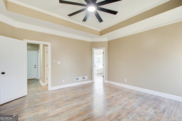 empty room with light wood-type flooring, a raised ceiling, visible vents, and baseboards