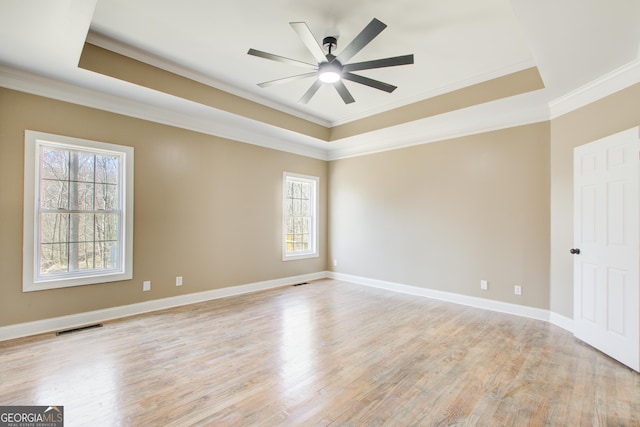 unfurnished room featuring a tray ceiling, light wood-style flooring, and visible vents