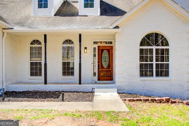 entrance to property featuring a porch, brick siding, and a shingled roof