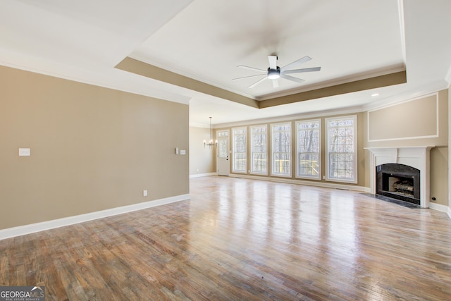 unfurnished living room with a tray ceiling, a fireplace with flush hearth, wood finished floors, baseboards, and ceiling fan with notable chandelier