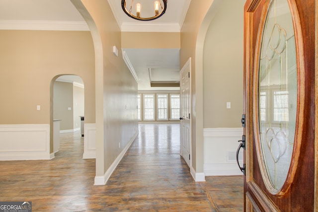 entrance foyer with arched walkways, crown molding, a decorative wall, dark wood-type flooring, and wainscoting