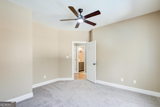 spare room with a ceiling fan, light colored carpet, and baseboards