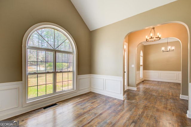 spare room with a wainscoted wall, wood finished floors, visible vents, vaulted ceiling, and an inviting chandelier