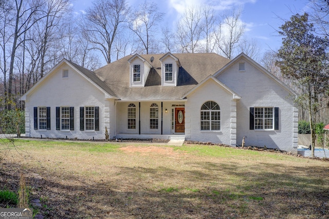 view of front of house with covered porch, a front lawn, roof with shingles, and brick siding