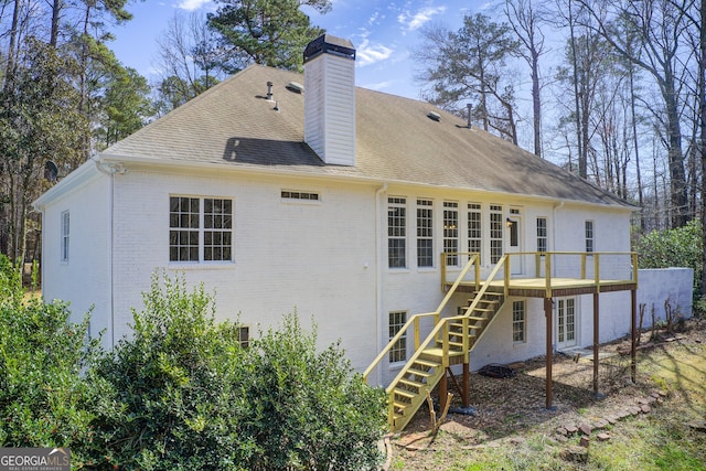 back of house featuring brick siding, roof with shingles, a chimney, stairway, and a deck