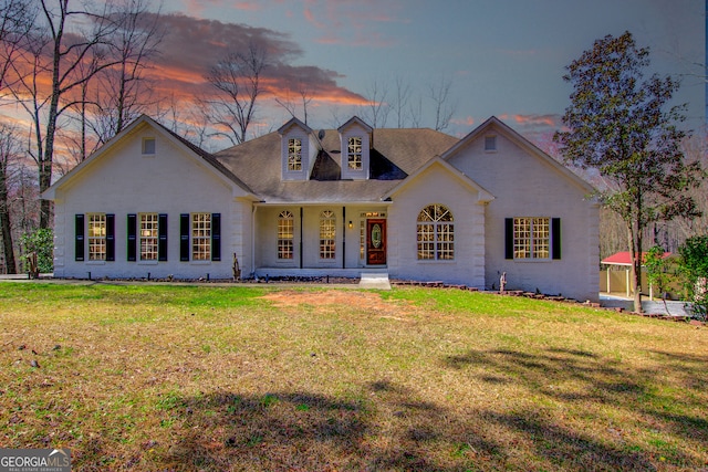 view of front of home with covered porch, brick siding, and a yard