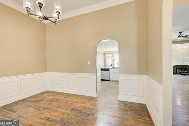 unfurnished dining area with arched walkways, ceiling fan with notable chandelier, a fireplace, wood finished floors, and crown molding