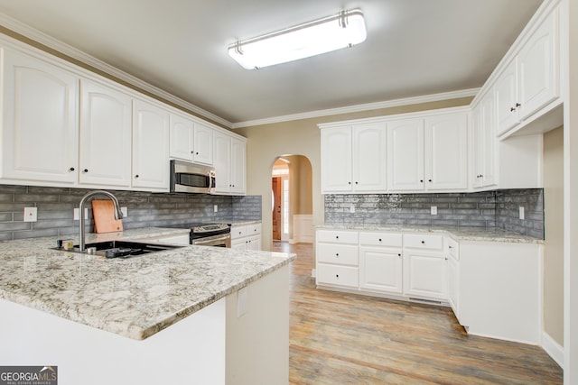 kitchen with arched walkways, appliances with stainless steel finishes, a peninsula, light stone countertops, and a sink