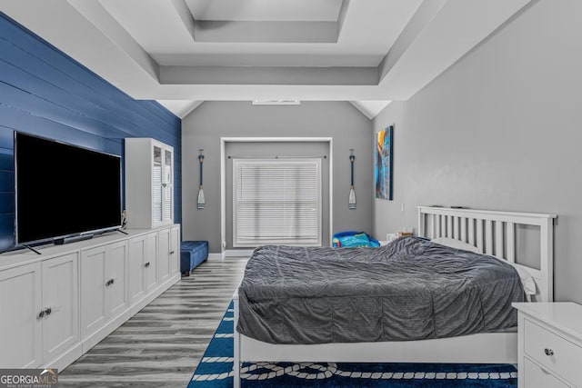 bedroom featuring a tray ceiling, light hardwood / wood-style flooring, and vaulted ceiling