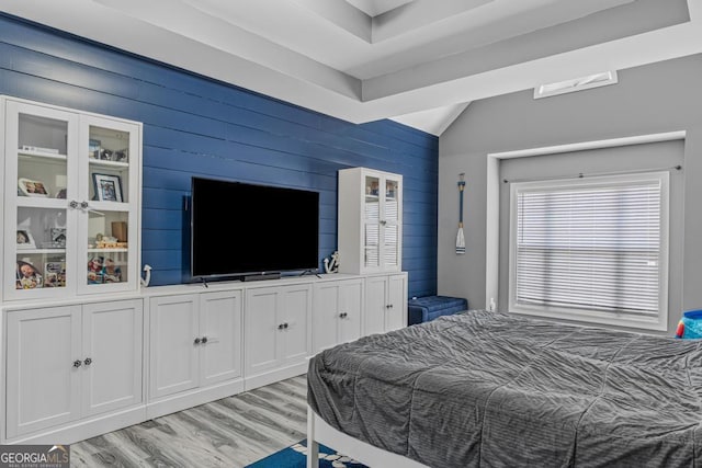 bedroom with wooden walls, light wood-type flooring, and lofted ceiling