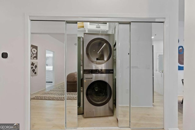 washroom with stacked washer / drying machine, wood finished floors, and laundry area