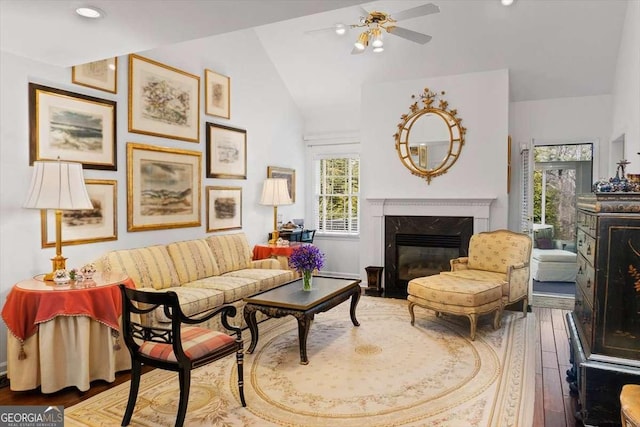 living room with ceiling fan, vaulted ceiling, wood-type flooring, and a fireplace